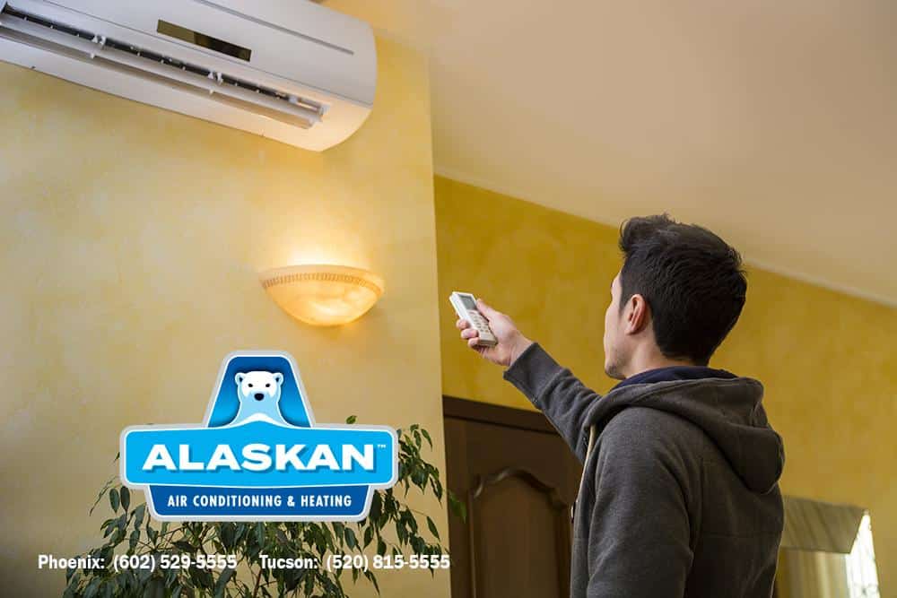 man pointing remote at split system mounted near ceiling with Alaskan AC logo and contact info